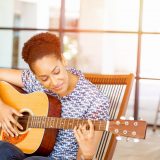 Portrait of smiling afro-american office worker sitting in offfice with guitar